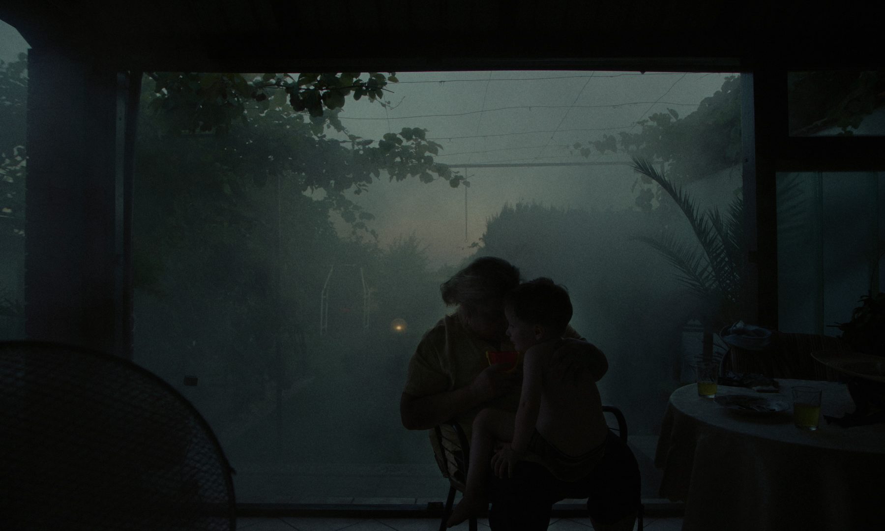 A woman and a child on a terrace, fog behind them at dusk
